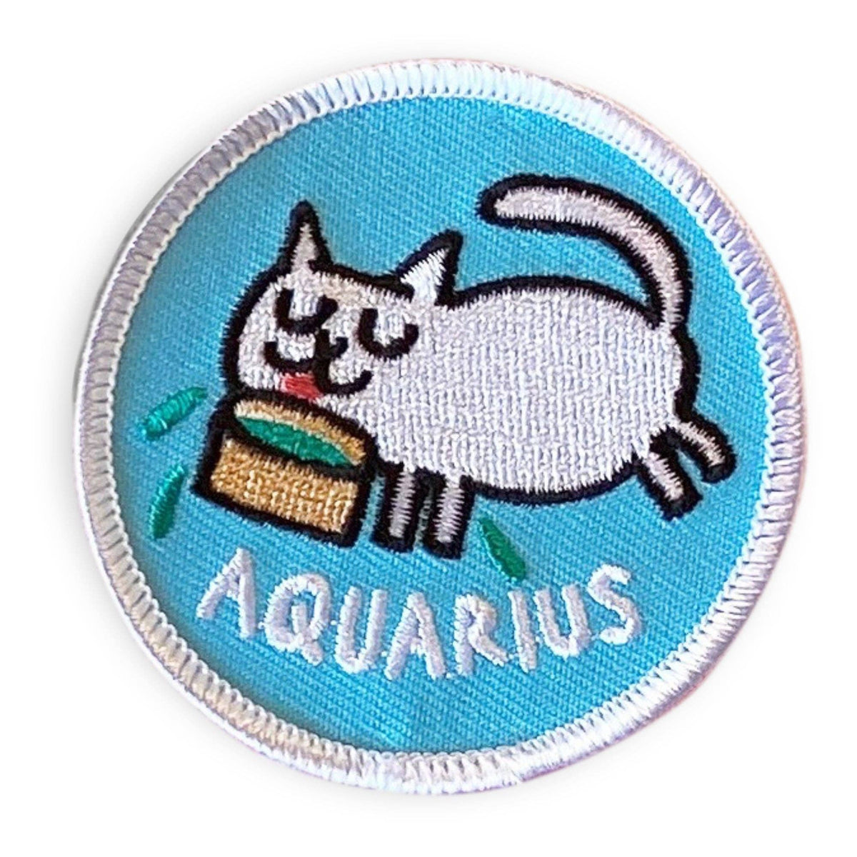 A circular embroidered patch featuring a white cat eating from a basket with the word 'AQUARIUS' below it, on a light blue background with a white stitched border.