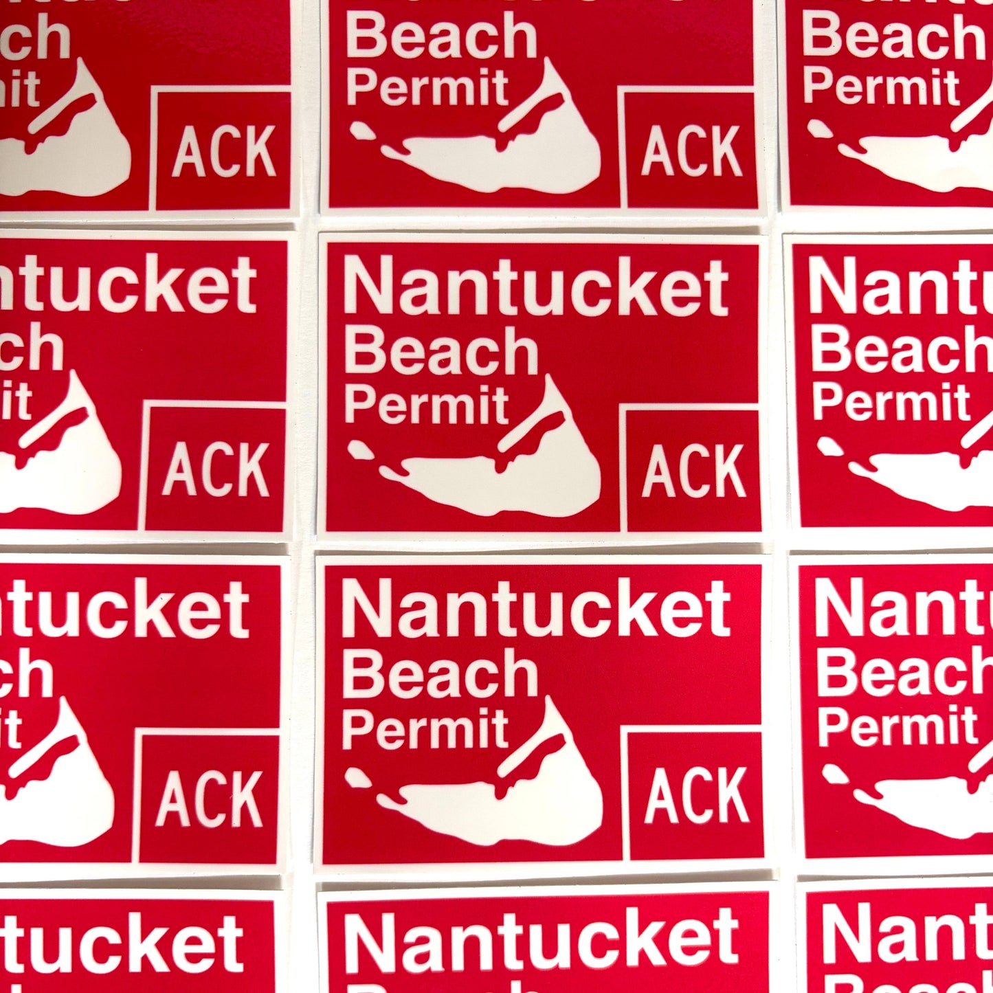 A close-up grid of red rectangular stickers printed with the text 'Nantucket Beach Permit' and a white shell logo, with 'ACK' in a box at the bottom right.