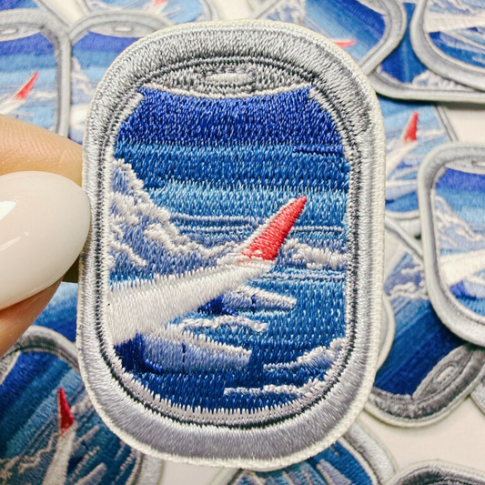 Embroidered patch of an airplane over water with a red tip, held by a hand.