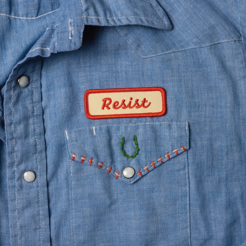 Blue denim shirt with 'Resist' patch on chest pocket
