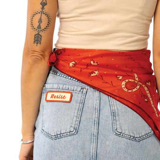 Person wearing a red bandana with patterns and a denim apron with a 'Resist' patch.