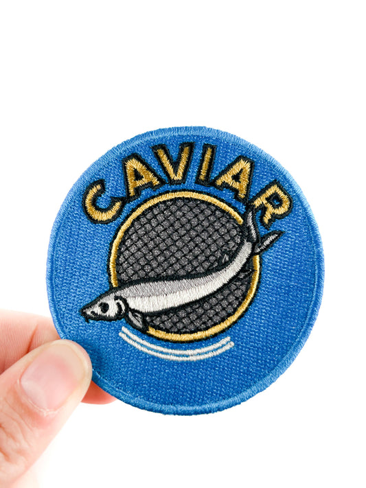 Circular patch with 'CAVIAR' text and a fish design held by a hand on a white background
