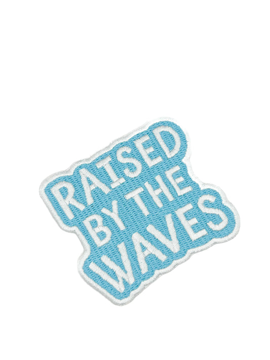 Embroidered patch with 'Raised by the Waves' text on a white background