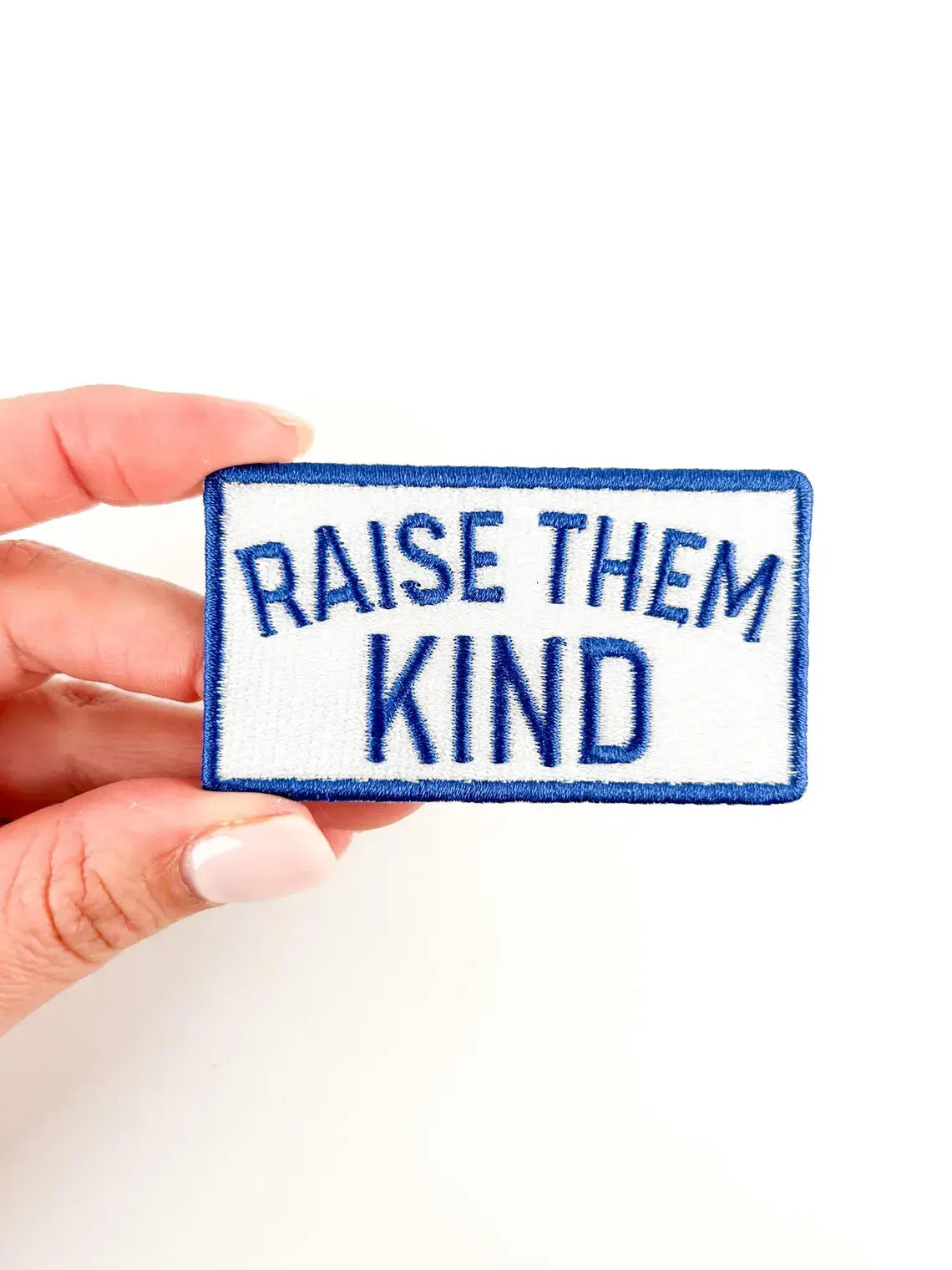 Patch with 'Raise Them Kind' text held by a hand on a white background