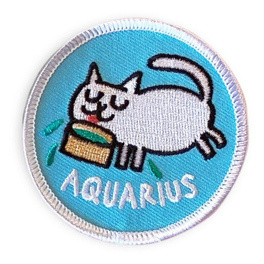 A circular embroidered patch featuring a white cat eating from a basket with the word 'AQUARIUS' below it, on a light blue background with a white stitched border.