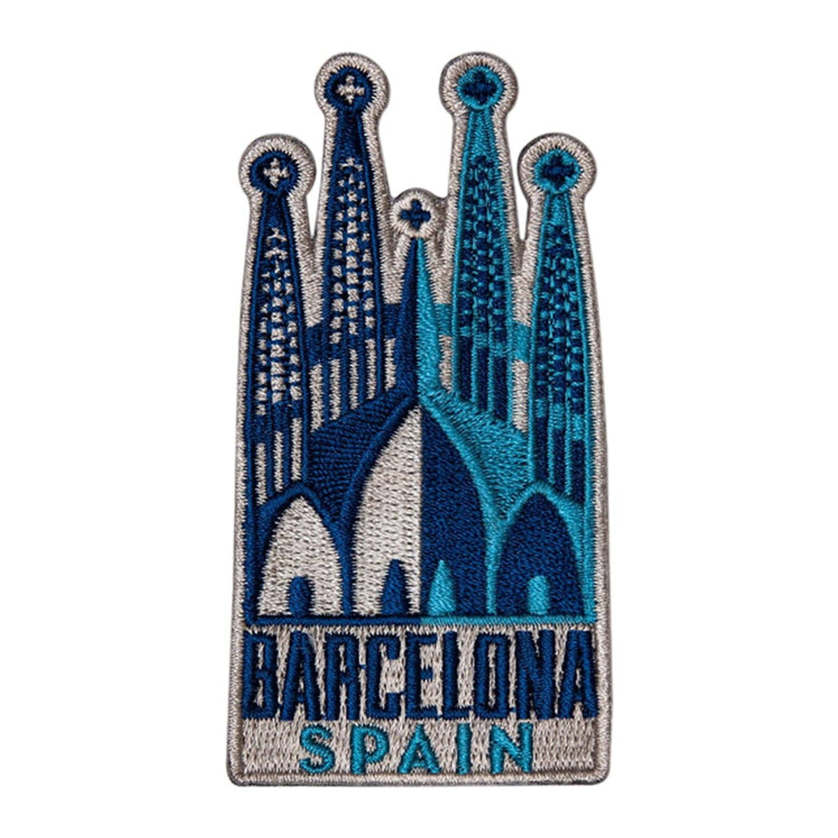 An embroidered patch featuring the Sagrada Familia in Barcelona, Spain, with the text 'BARCELONA SPAIN' stitched at the bottom. The design uses shades of blue, teal, and white on a silver-gray embroidered border, set against a plain white background.