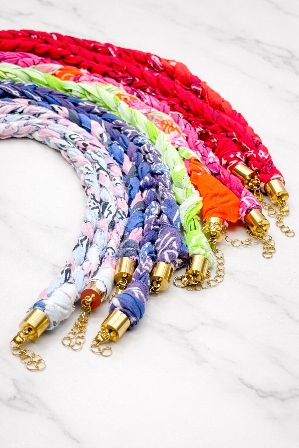Colorful braided bandana necklaces with gold ends on a white marble surface
