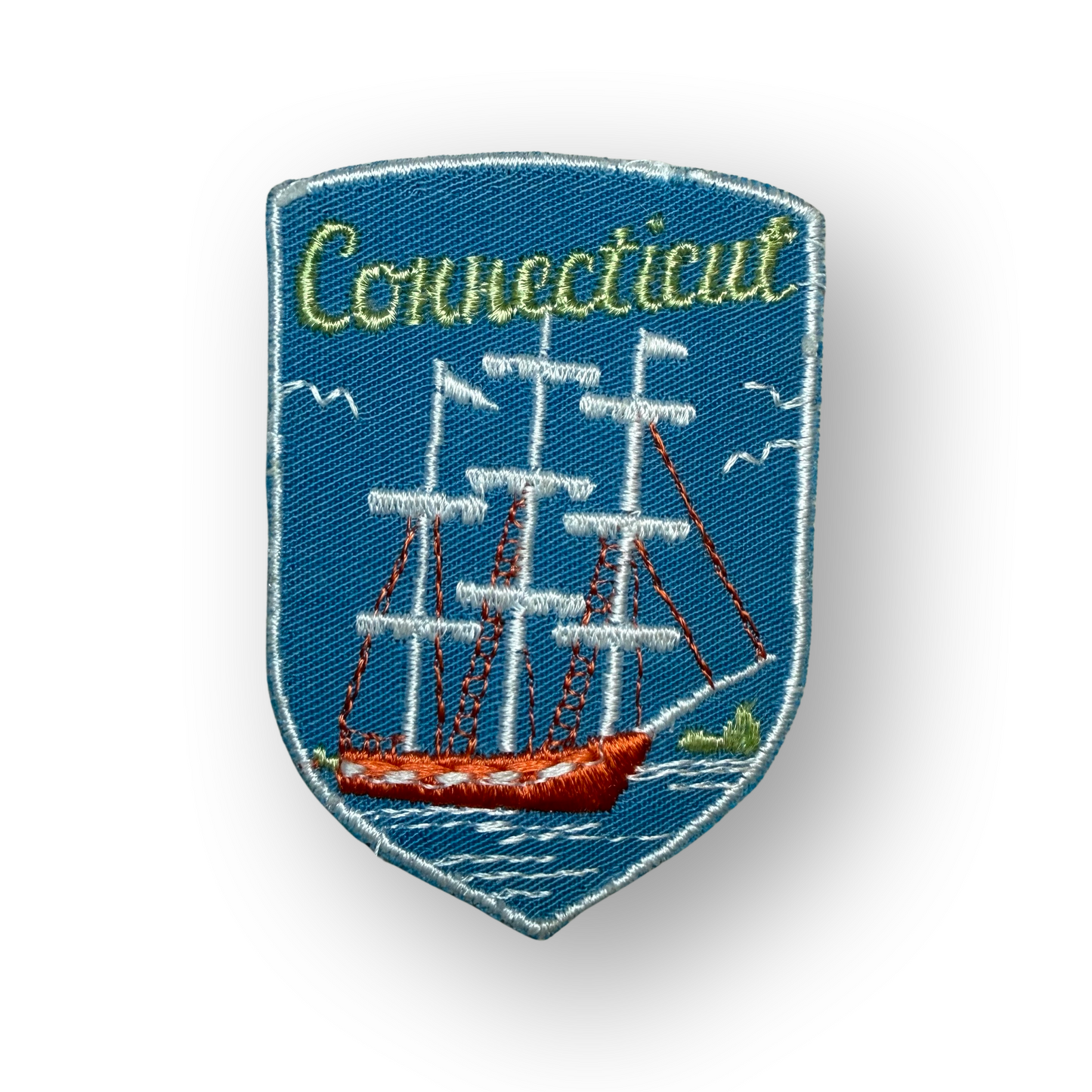 An embroidered shield-shaped patch featuring a blue background with a white sailing ship, red hull, and the word 'Connecticut' in yellow-green script at the top.