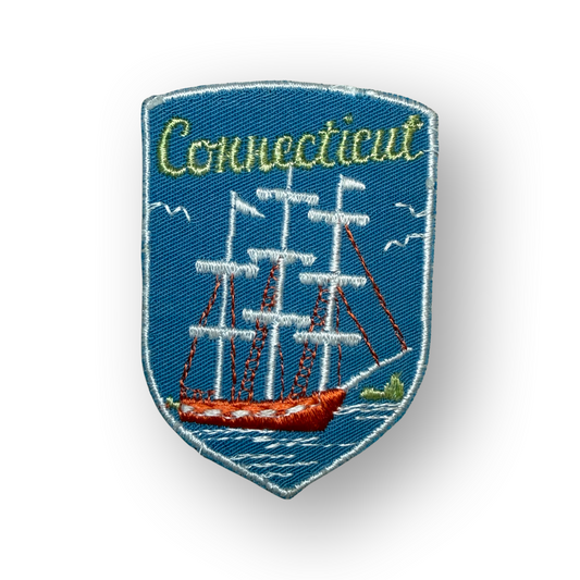 An embroidered shield-shaped patch featuring a blue background with a white sailing ship, red hull, and the word 'Connecticut' in yellow-green script at the top.