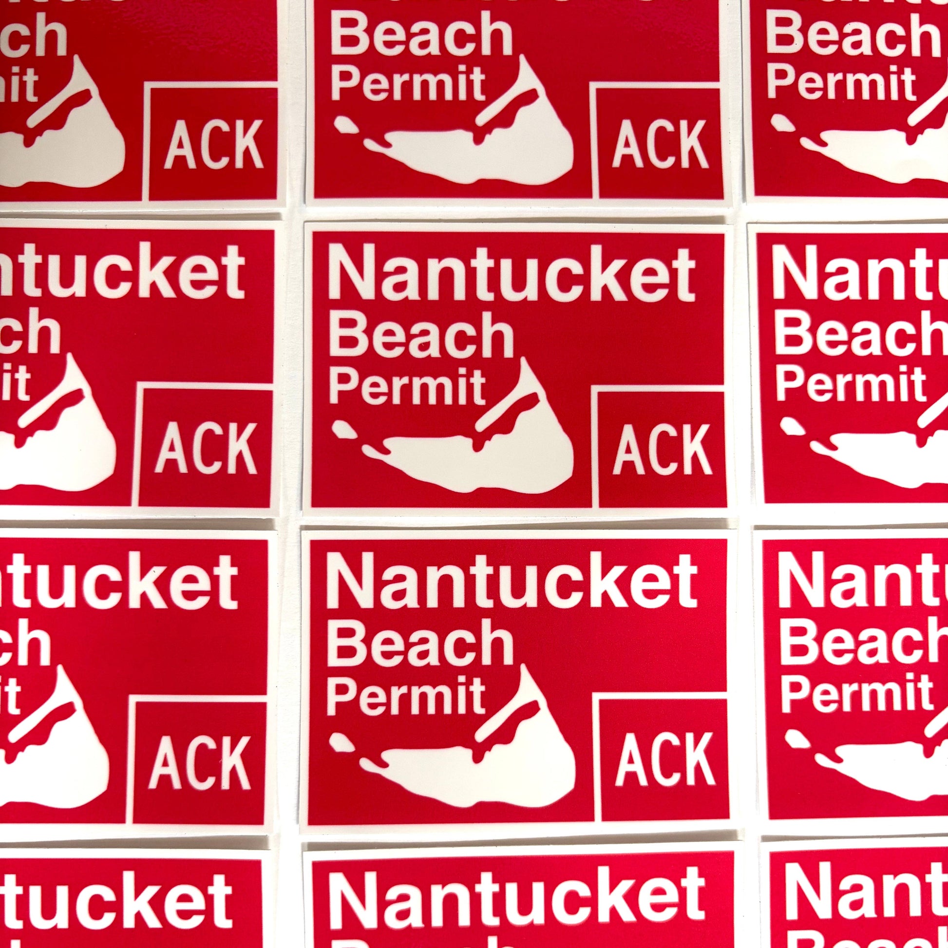 A close-up grid of red rectangular stickers printed with the text 'Nantucket Beach Permit' and a white shell logo, with 'ACK' in a box at the bottom right.