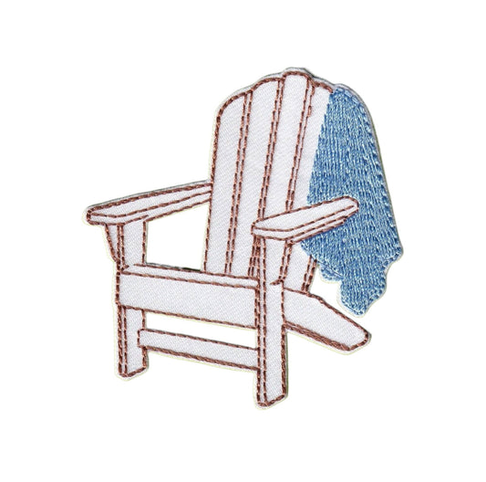 An embroidered patch depicting a white Adirondack chair with a blue textured throw blanket draped over one arm, outlined in brown stitching on a plain white background.