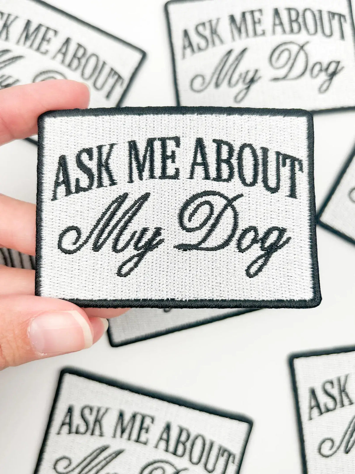 Patch with 'Ask Me About My Dog' text held by a hand on a white background
