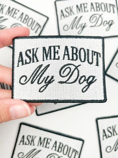 Patch with 'Ask Me About My Dog' text held by a hand on a white background