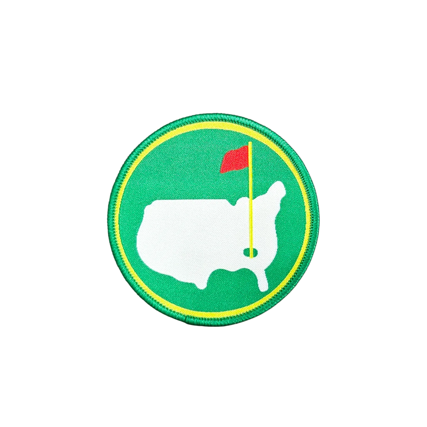 A circular embroidered patch featuring a white silhouette of the United States with a green golf flag and red flag on a green background, surrounded by a yellow border, placed on a white faux fur surface.
