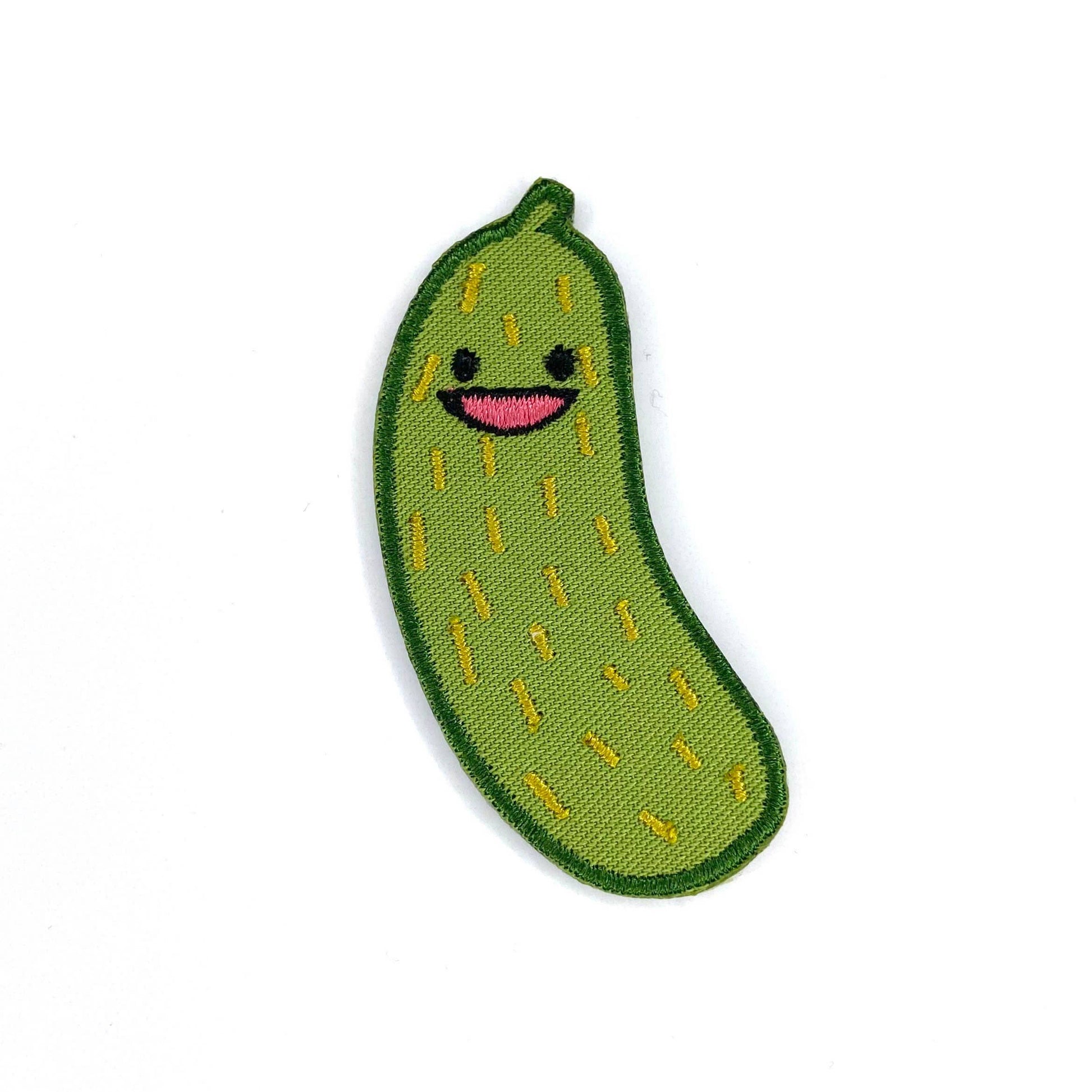 A cute embroidered patch shaped like a green cucumber with a smiling face, featuring yellow stitched details and a dark green border, set against a plain white background.