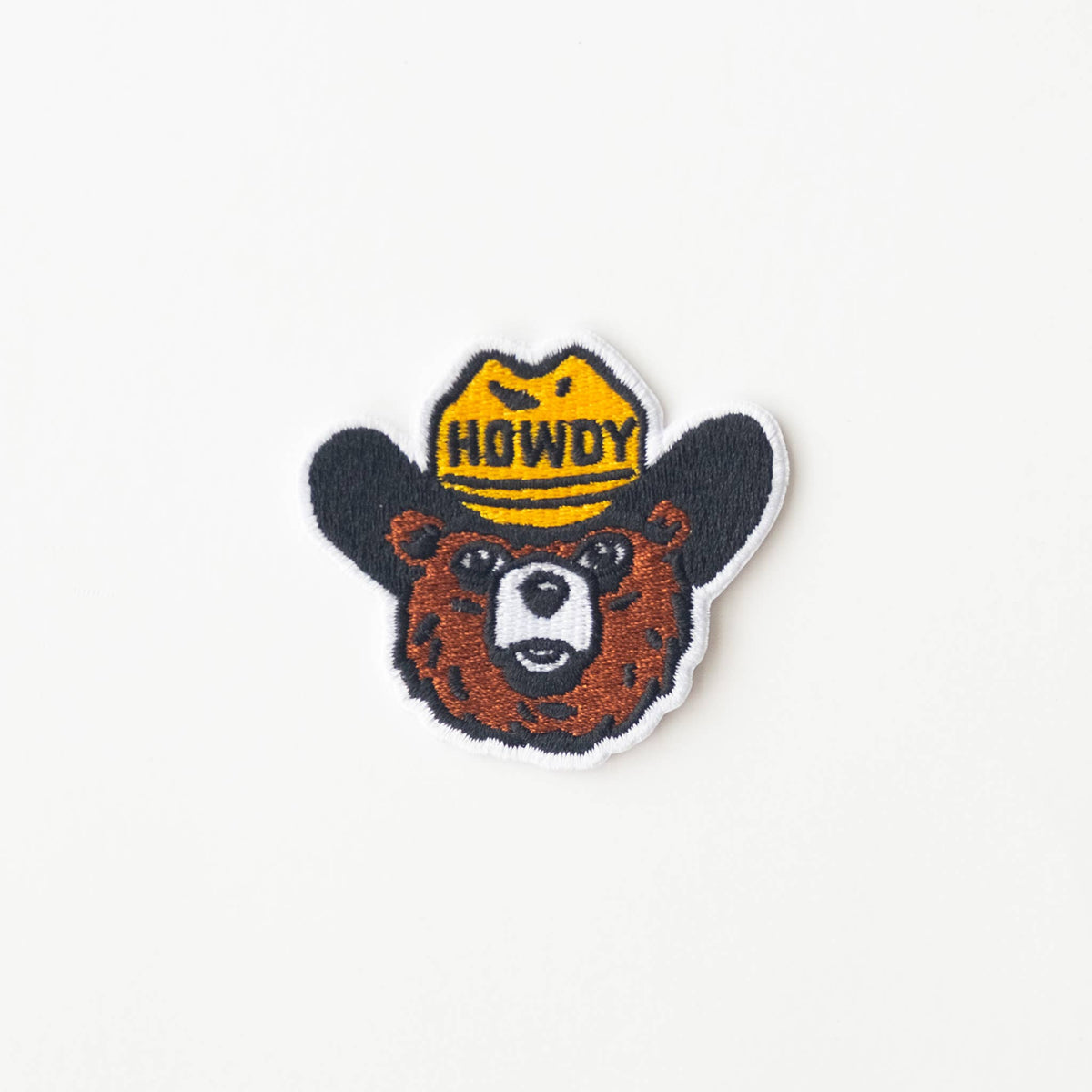 Embroidered patch of a bear wearing a 'Howdy' hat on a white background