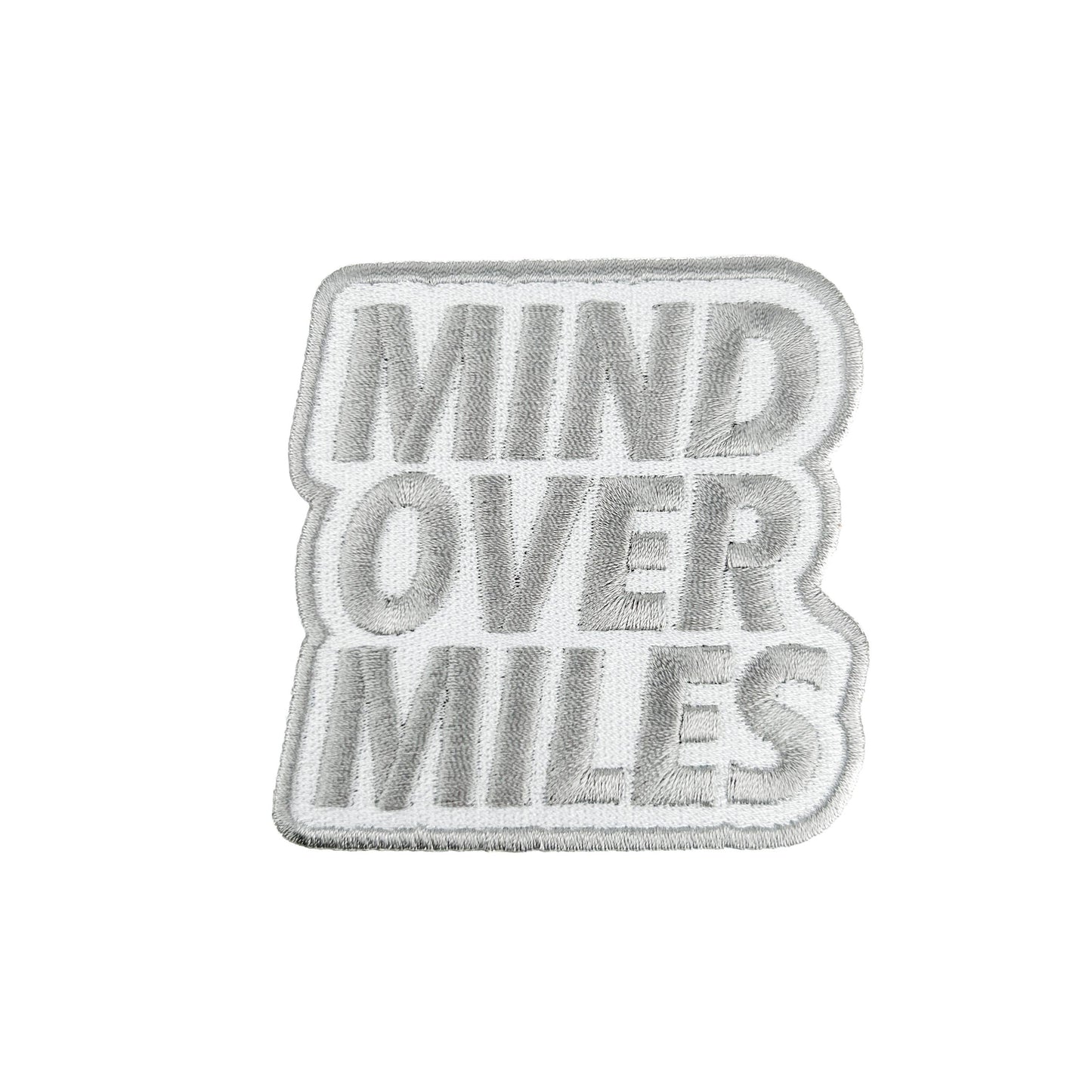 A rectangular embroidered patch with the words 'MIND OVER MILES' in raised gray lettering on a white background, finished with a gray border.