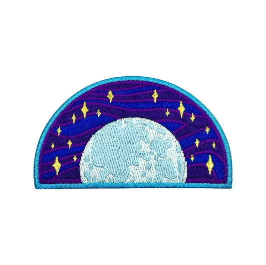 An embroidered patch depicting a celestial night sky with a large light blue moon and yellow stars against a purple and blue starry background, finished with a turquoise border.