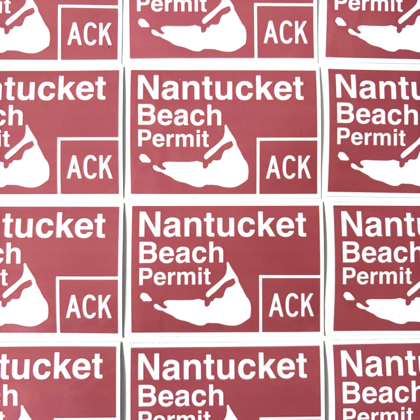 A close-up repeating pattern of rectangular red stickers with white text reading 'Nantucket Beach Permit' and a white silhouette of Nantucket Island, with 'ACK' also printed in a box.