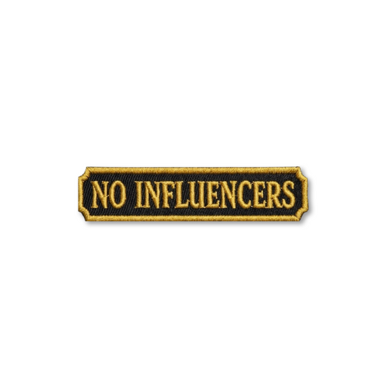 An embroidered rectangular patch with the words 'NO INFLUENCERS' in gold lettering on a black background, outlined with a gold border, shown on a plain white background.