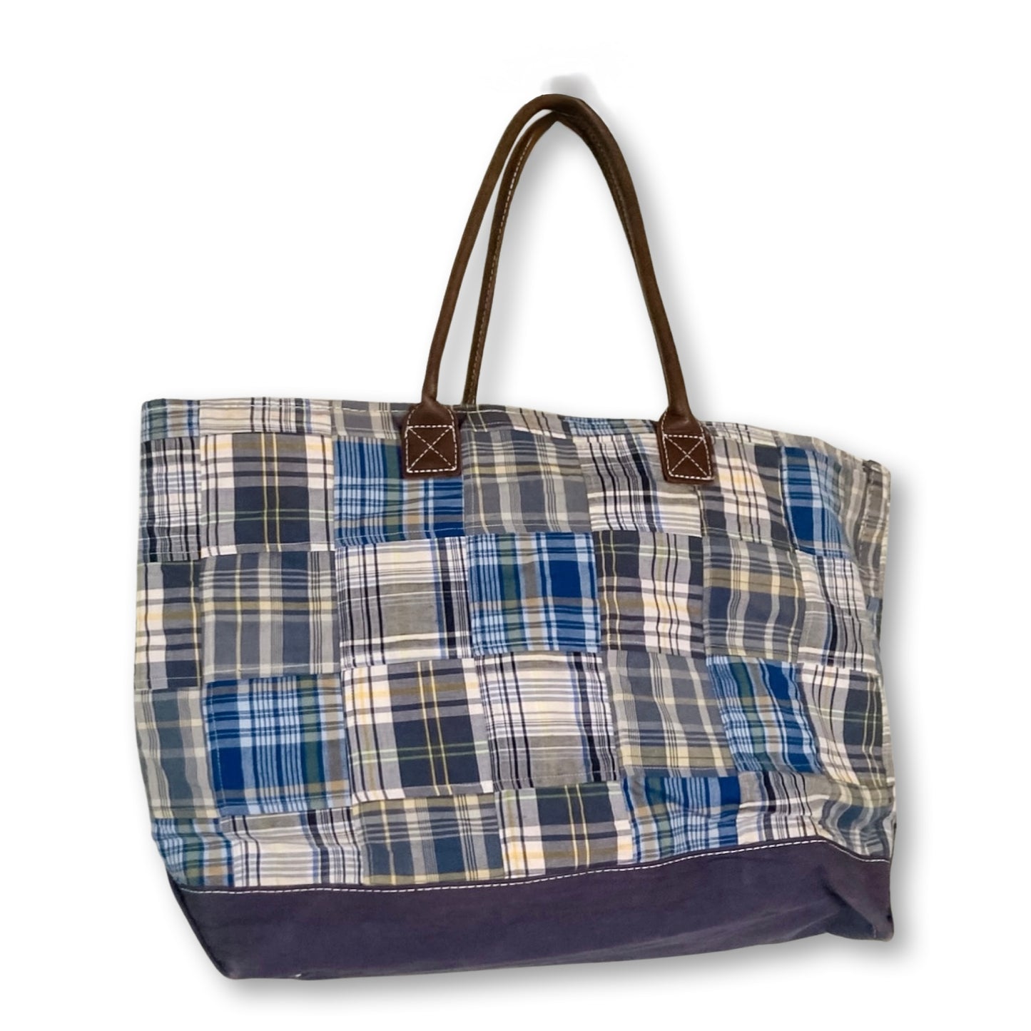 A patchwork plaid tote bag featuring blue, navy, beige, and white fabric squares, with dark brown leather handles and a solid navy bottom panel.
