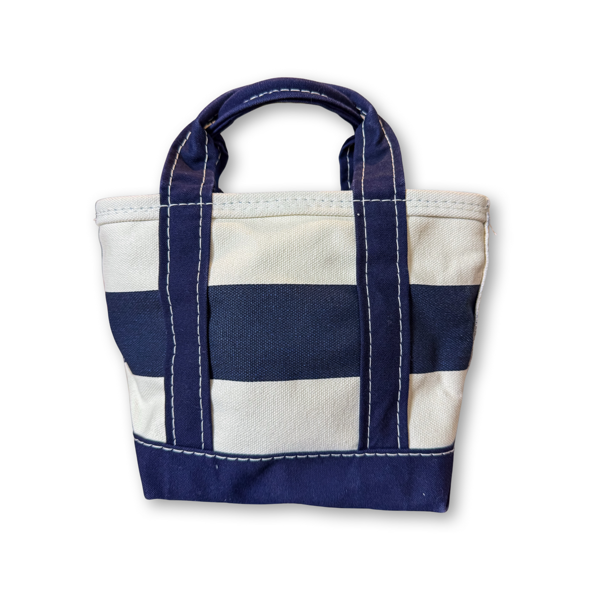 A small canvas tote bag with horizontal navy blue and off-white stripes, featuring thick navy handles and white contrast stitching, shown on a plain white background.
