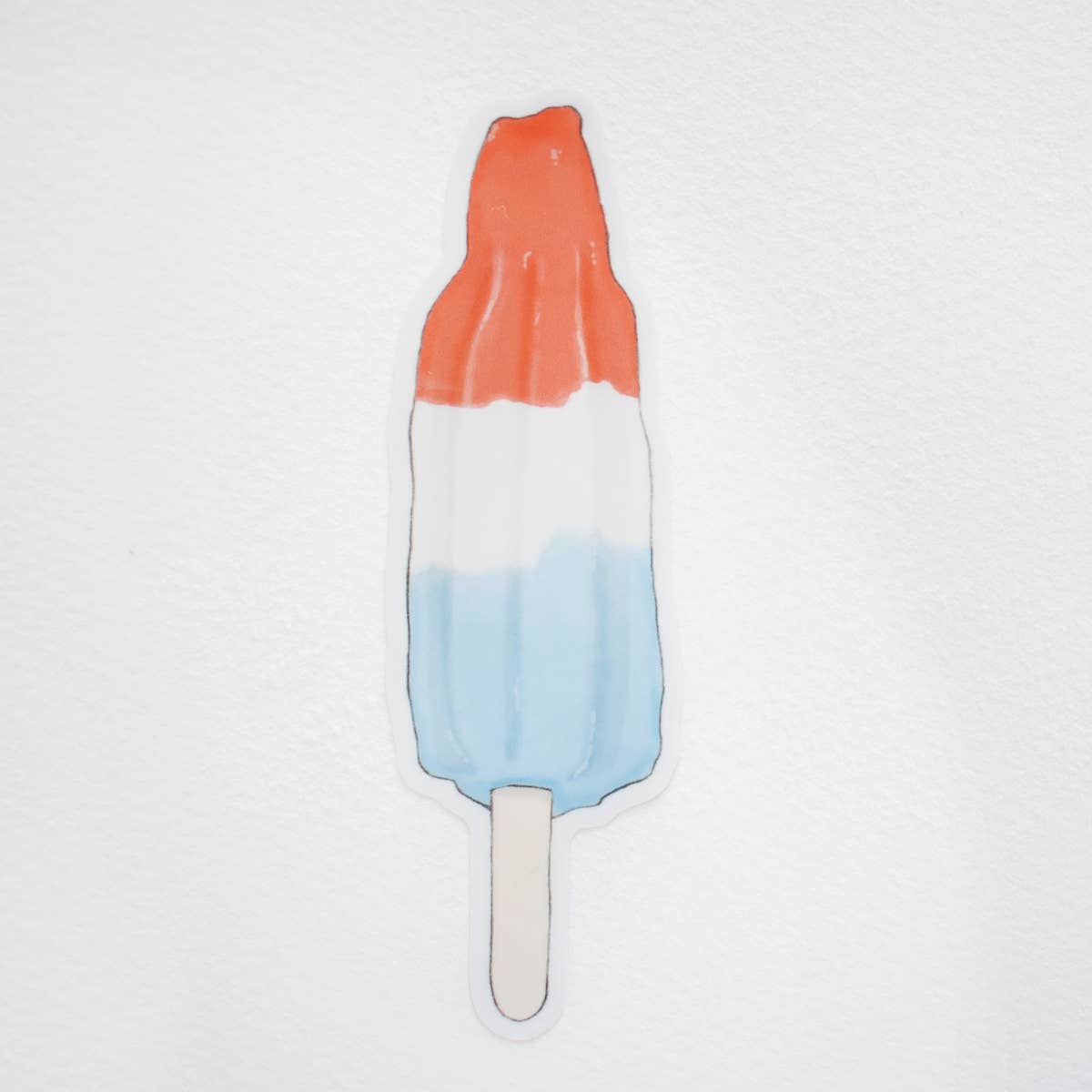A die-cut sticker shaped like a popsicle with horizontal red, white, and blue layers on a stick, shown against a textured white background.