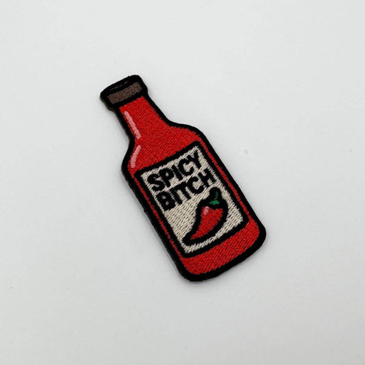 Embroidered patch of a red bottle labeled 'Spicy Bitch' on a white background