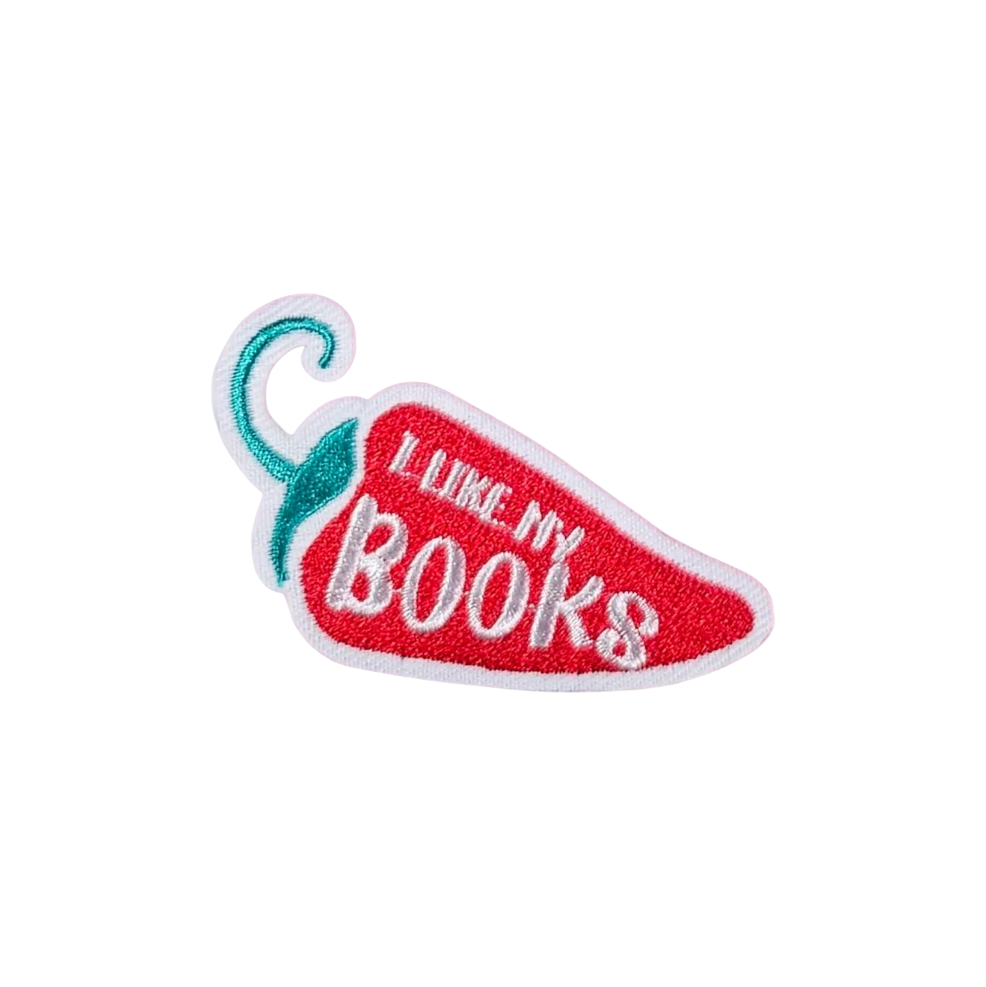 An embroidered chili pepper-shaped patch with the phrase 'I LIKE MY BOOKS' in white lettering on a red background, with a teal stem and white border, placed on a white faux fur surface.