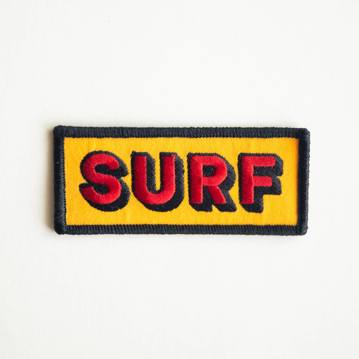 A rectangular embroidered patch with the word 'SURF' in red letters outlined in black on a bright yellow background, finished with a black stitched border, shown on a plain white background.