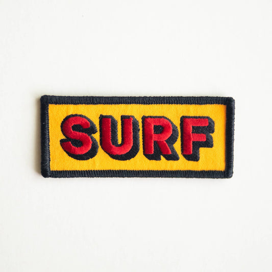 A rectangular embroidered patch with the word 'SURF' in red letters outlined in black on a bright yellow background, finished with a black stitched border, shown on a plain white background.