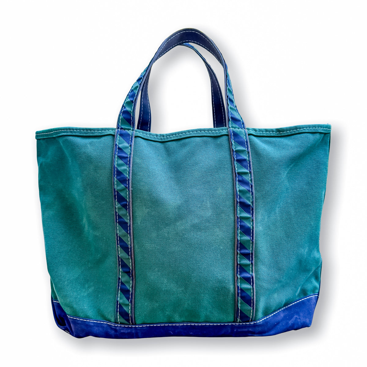 A teal canvas tote bag with dark blue handles, trim, and bottom panel, shown against a plain white background.
