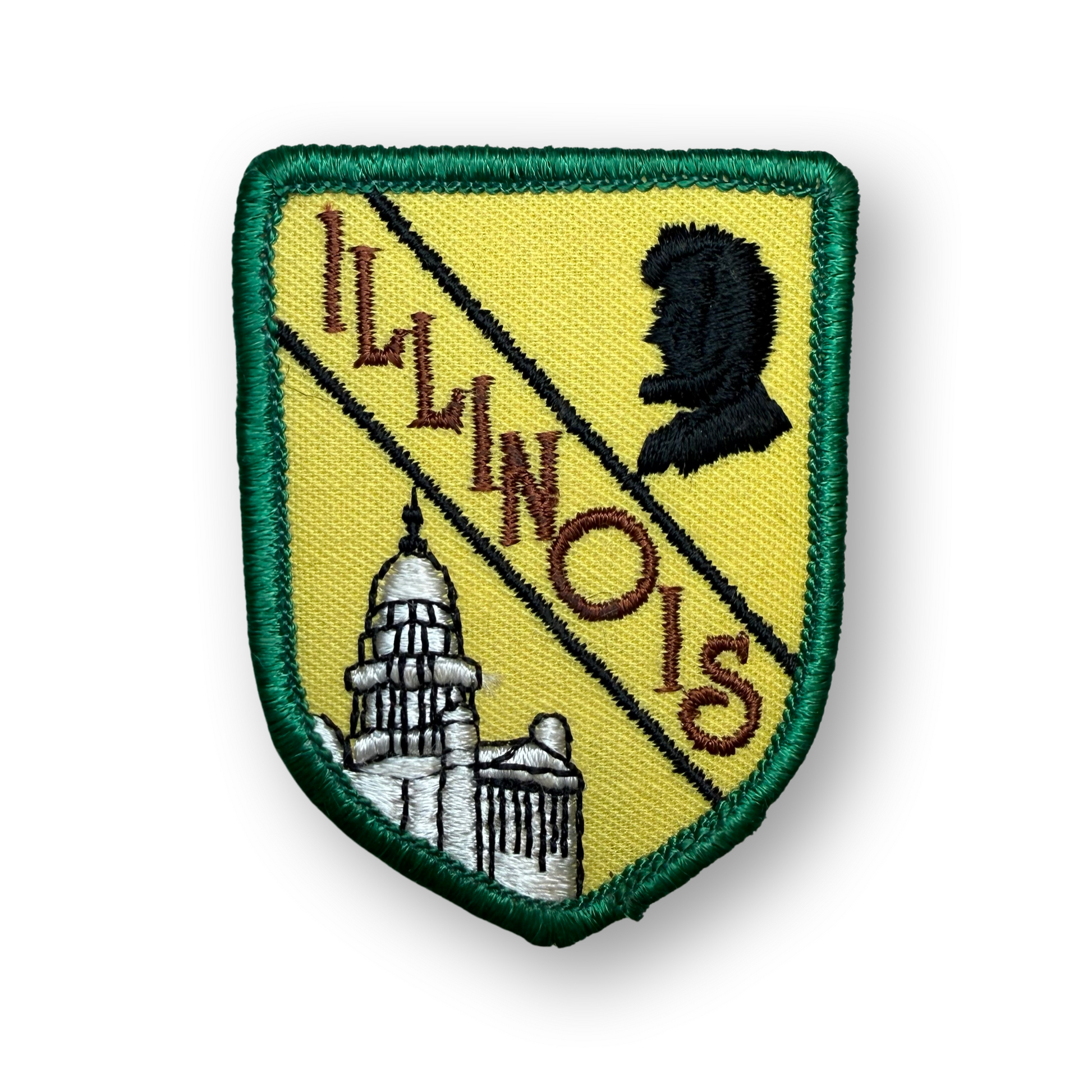 An embroidered Illinois state shield patch with a green border, yellow field, diagonal black stripe, brown 'ILLINOIS' text, a black silhouette profile, and a white-and-gray capitol building, shown on a white background.
