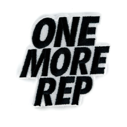 A black embroidered patch with the phrase 'ONE MORE REP' in bold, stylized lettering on a white background.