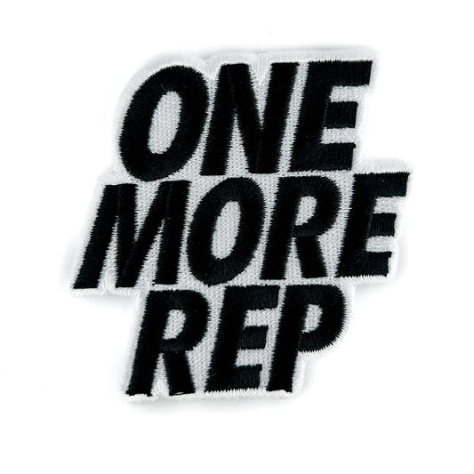A black embroidered patch with the phrase 'ONE MORE REP' in bold, stylized lettering on a white background.