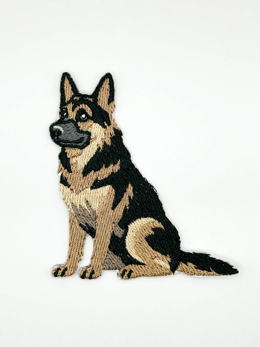 An embroidered patch of a sitting German Shepherd dog, featuring black and tan stitching on a plain white background.