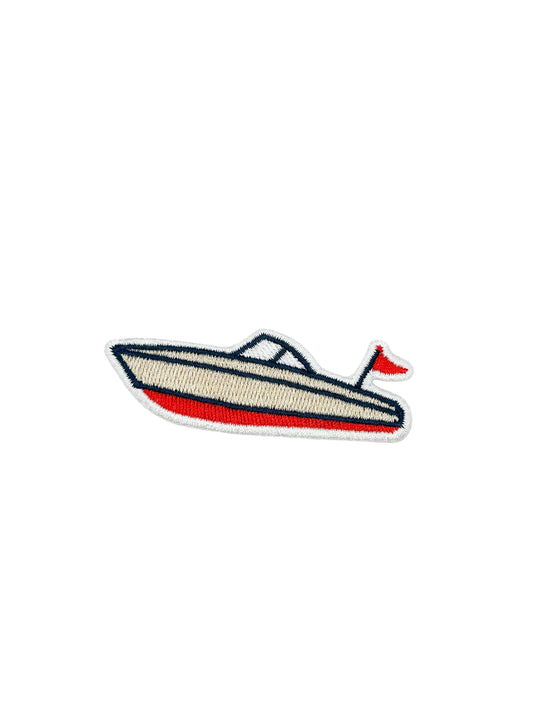An embroidered patch of a speedboat with a cream-colored hull, a red lower stripe, dark blue trim, and a small red flag on a white background.