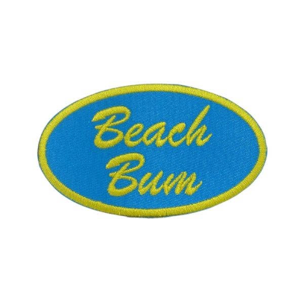 An oval embroidered patch with a bright blue background, yellow border, and yellow script text reading 'Beach Bum' on a plain white background.