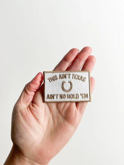 Hand holding a patch with text and a horseshoe symbol against a plain background