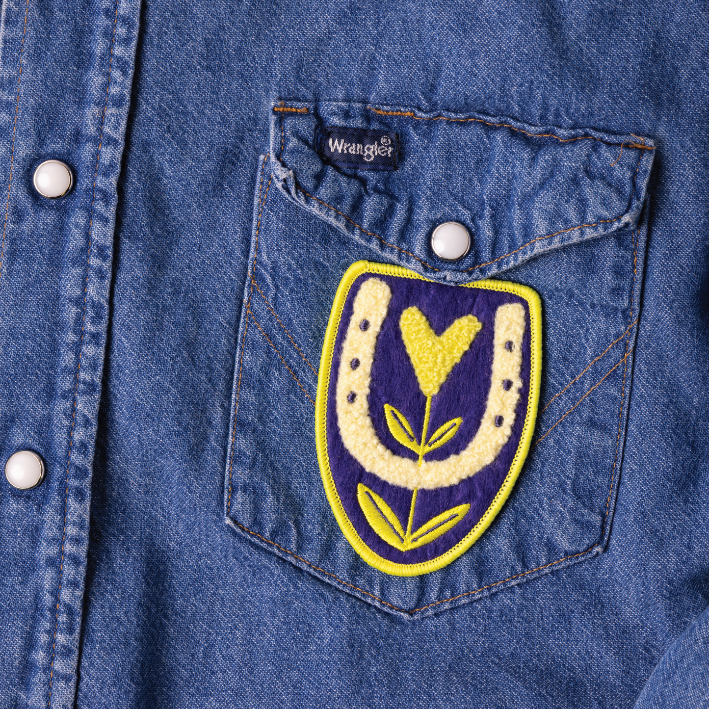 Denim pocket with embroidered patch featuring a yellow flower on a blue denim background