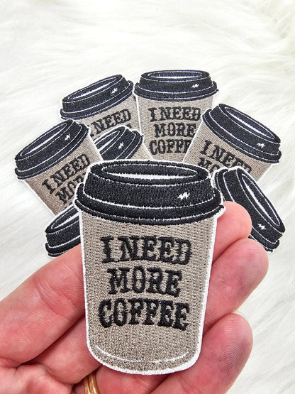 Patch of a coffee cup with 'I Need More Coffee' text held in a hand.