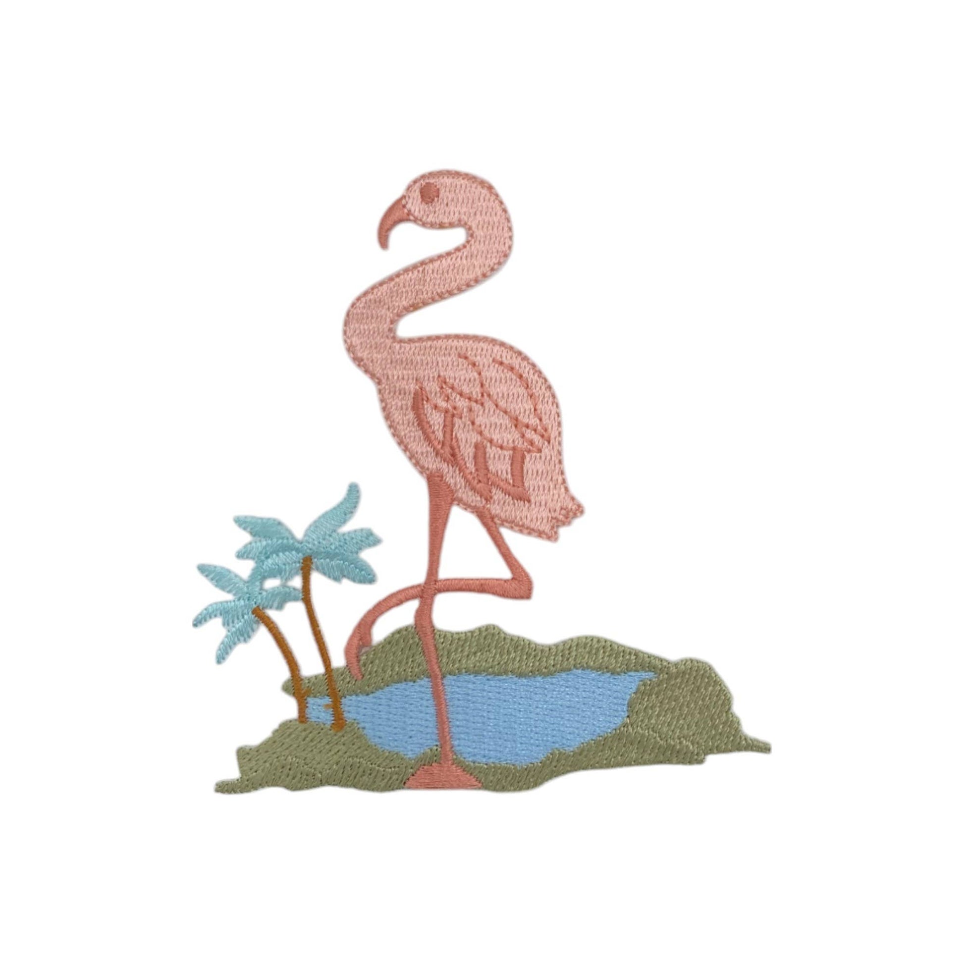 An embroidered patch featuring a pink flamingo standing on a patch of green grass next to a small blue pond, with two light blue palm trees, on a plain white background.