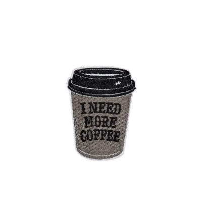 Coffee cup patch with 'I Need More Coffee' text on a pink cutting mat.
