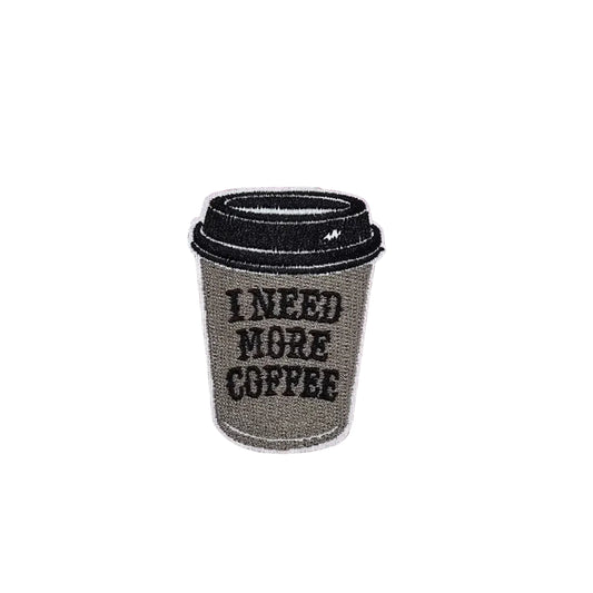 Coffee cup patch with 'I Need More Coffee' text on a pink cutting mat.
