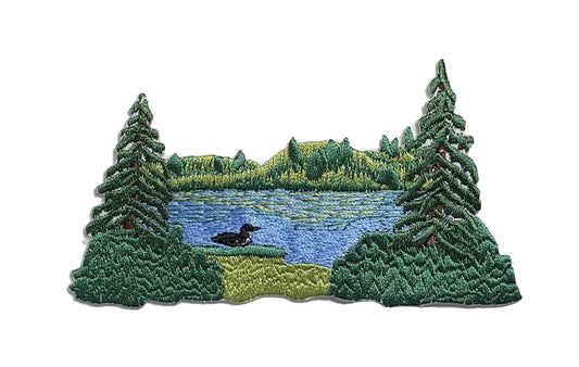 Embroidered patch of a forest lake scene with trees and a duck.