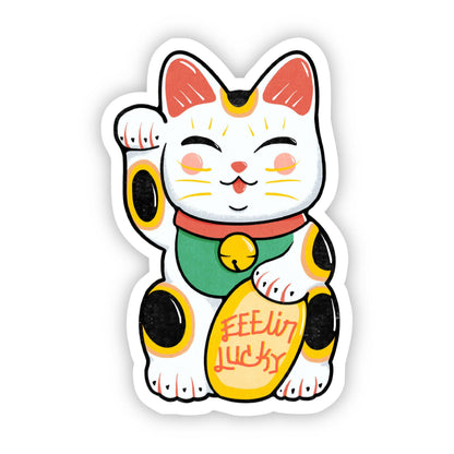 A die-cut sticker featuring a cartoon Maneki-neko lucky cat with one raised paw, holding a gold coin that reads 'FEEL IT LUCKY'. The cat is white with pink inner ears, black spots, a green collar, and a red bell, shown on a plain white background.