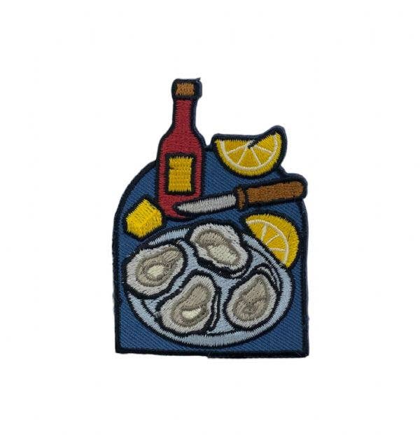 Embroidered patch with oysters, bottle, and lemon slices on a white background