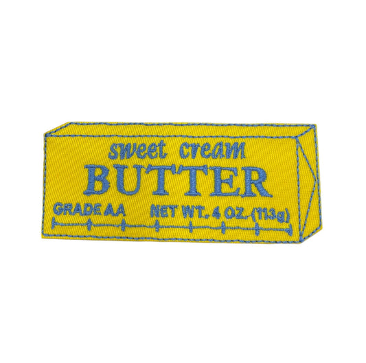 A yellow rectangular patch designed to look like a butter stick, with blue embroidered text reading 'sweet cream BUTTER GRADE AA NET WT. 4 OZ.