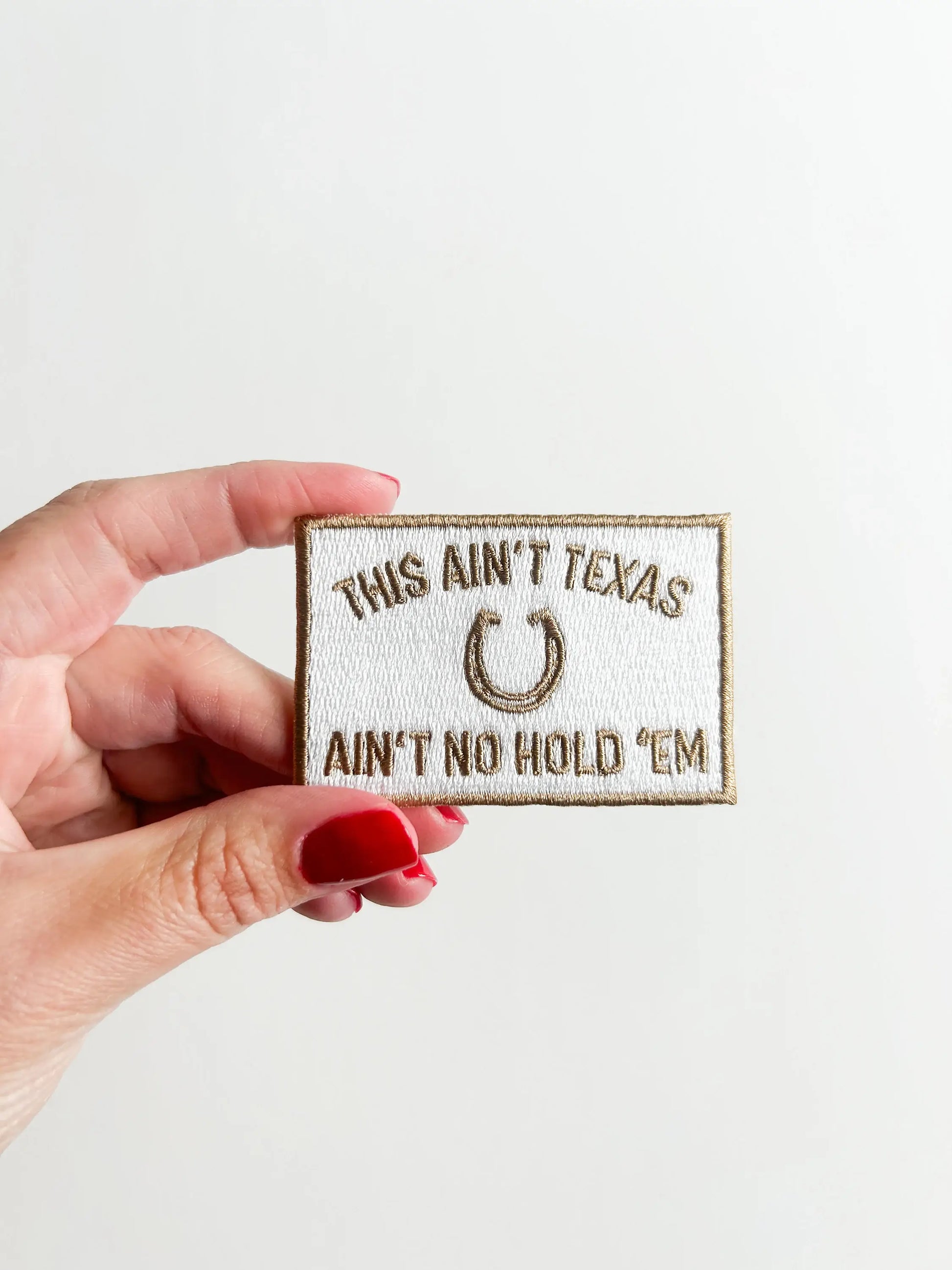 Hand holding a patch with text and a horseshoe symbol on a light background
