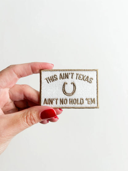 Hand holding a patch with text and a horseshoe symbol on a light background